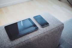Two communications devices - a tablet and smartphone on a sofa
